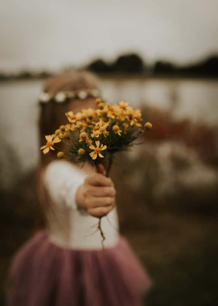 Emosionele Meisie wat Geel Blomme Vashou Prent Muurpapier