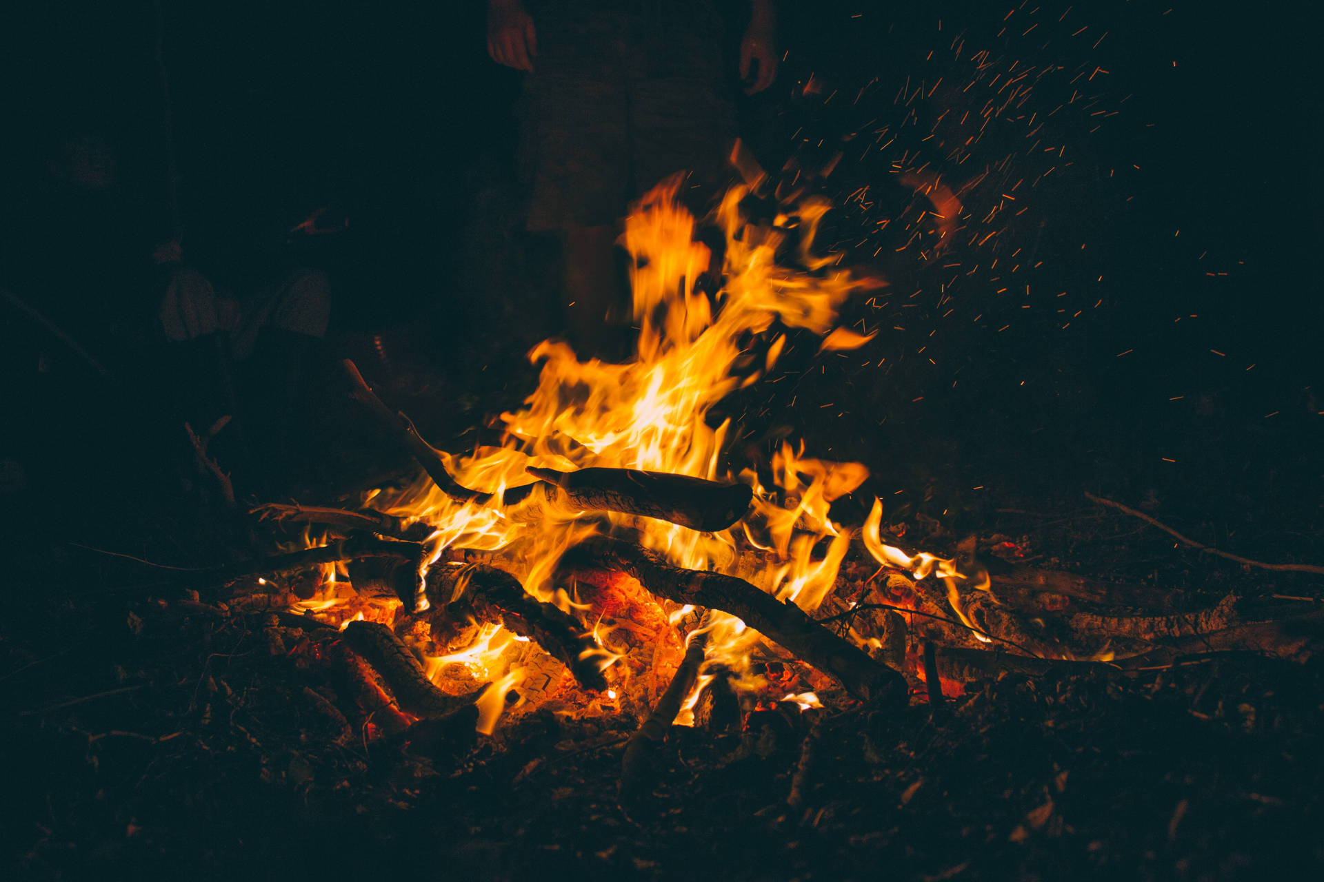 Kampvuur met vlamende oranje vlamme wat vuurhoutjies brand en die donker nag in die bos verlig.