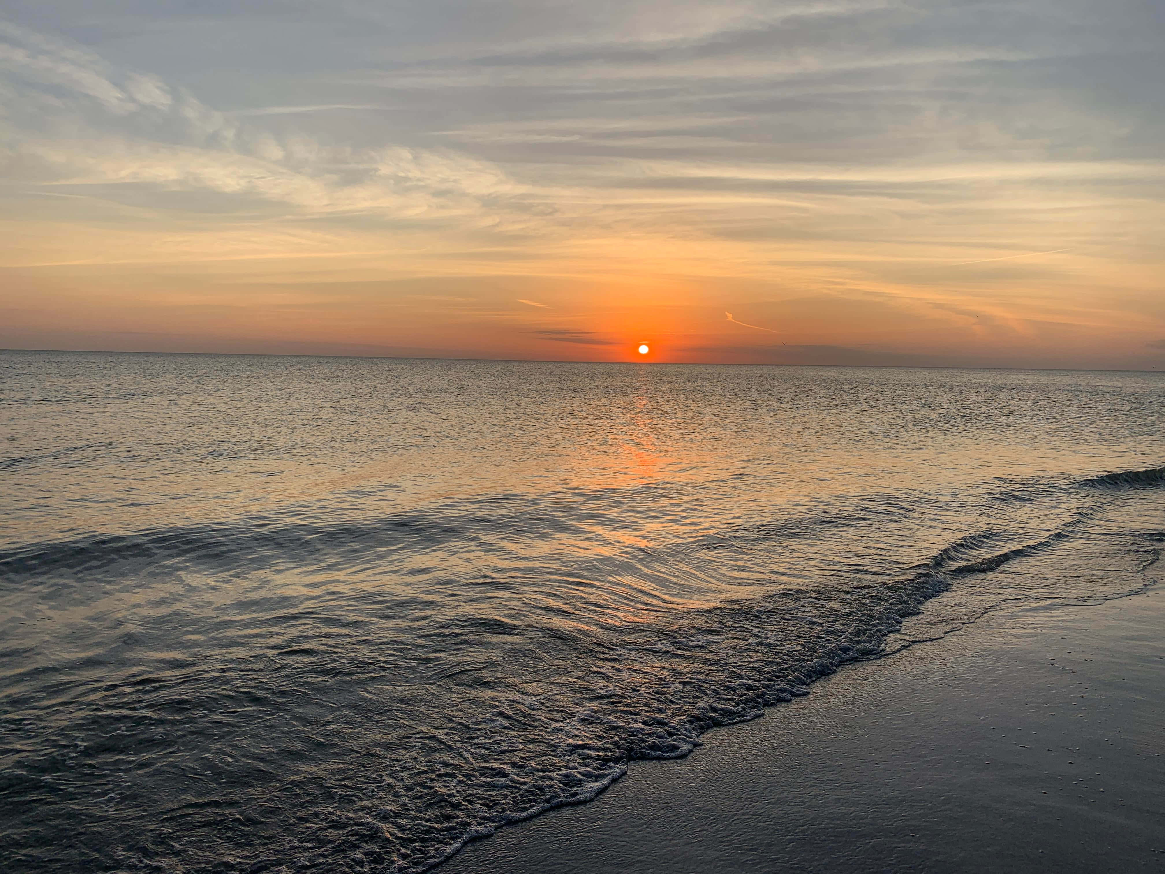 Geniet van die briljante kleure van 'n strandsononder Muurpapier