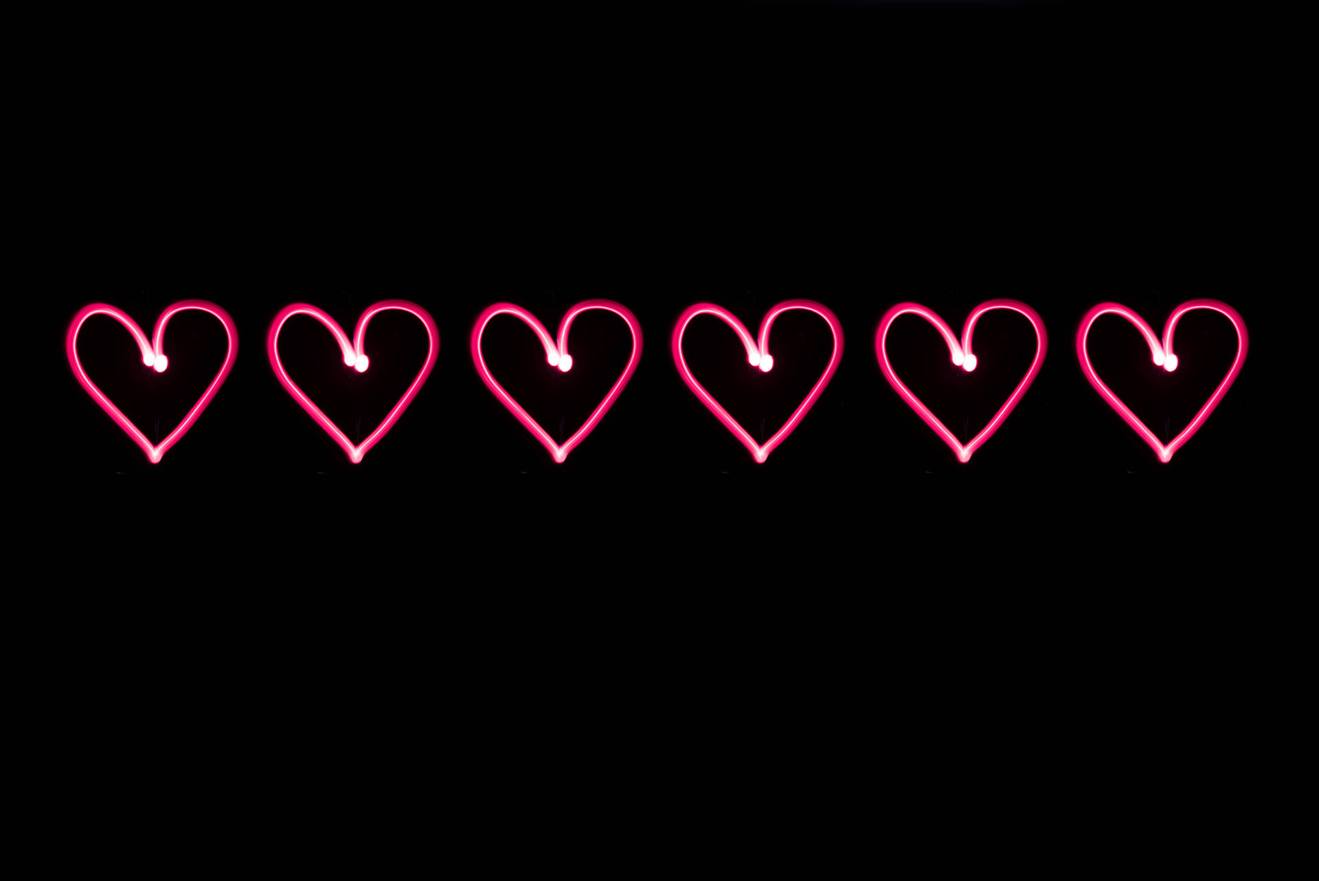 Pienk neonharte geteken op 'n swart agtergrond vir Valentynsdag. Digitale kuns vir jou liefde.