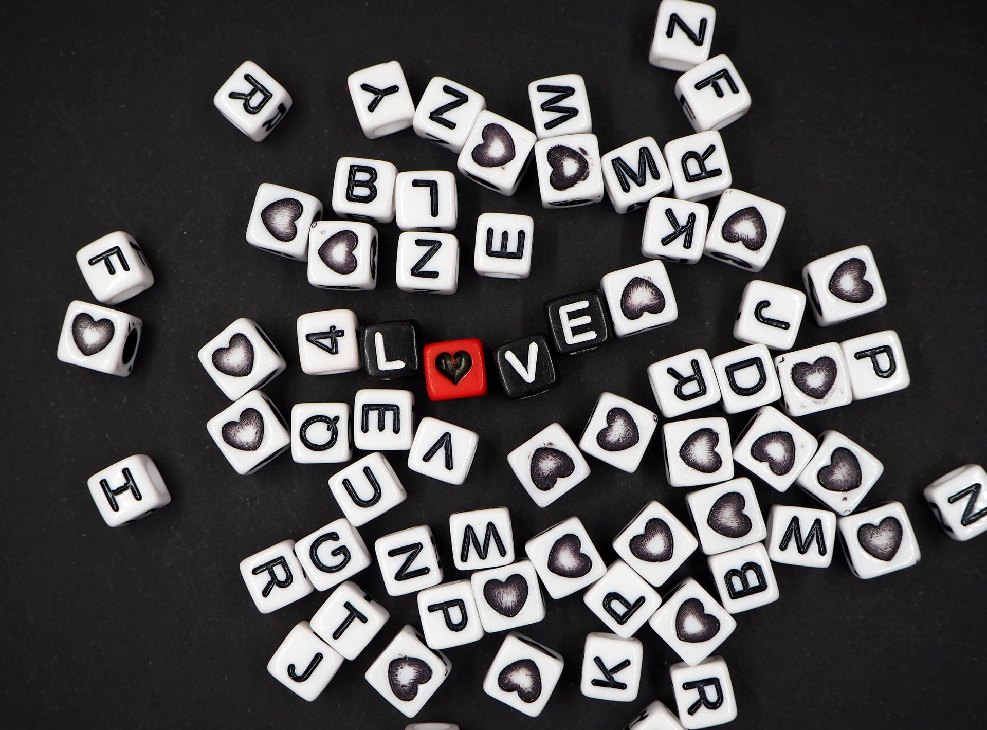Swart dobbelstene wat die woord "liefde" vorm met 'n hart wat die "O" vervang en verspreide letters van wit dobbelstene op 'n swart oppervlak vir Hartedag.