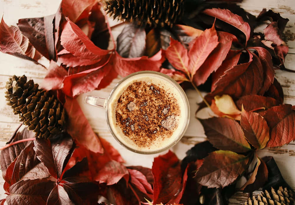 'n koppie koffie omring deur blare en dennekeëls Muurpapier