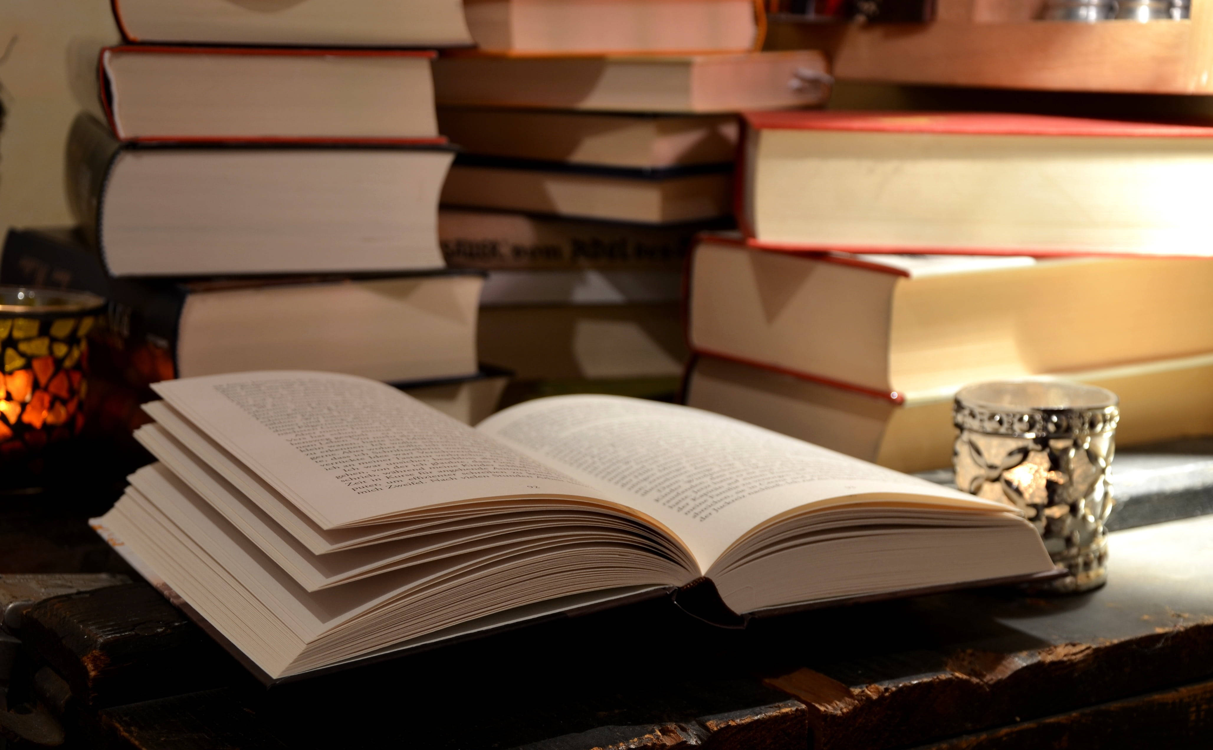 'n Oop boek op 'n lessenaar, omring deur ander naslaanboeke Muurpapier