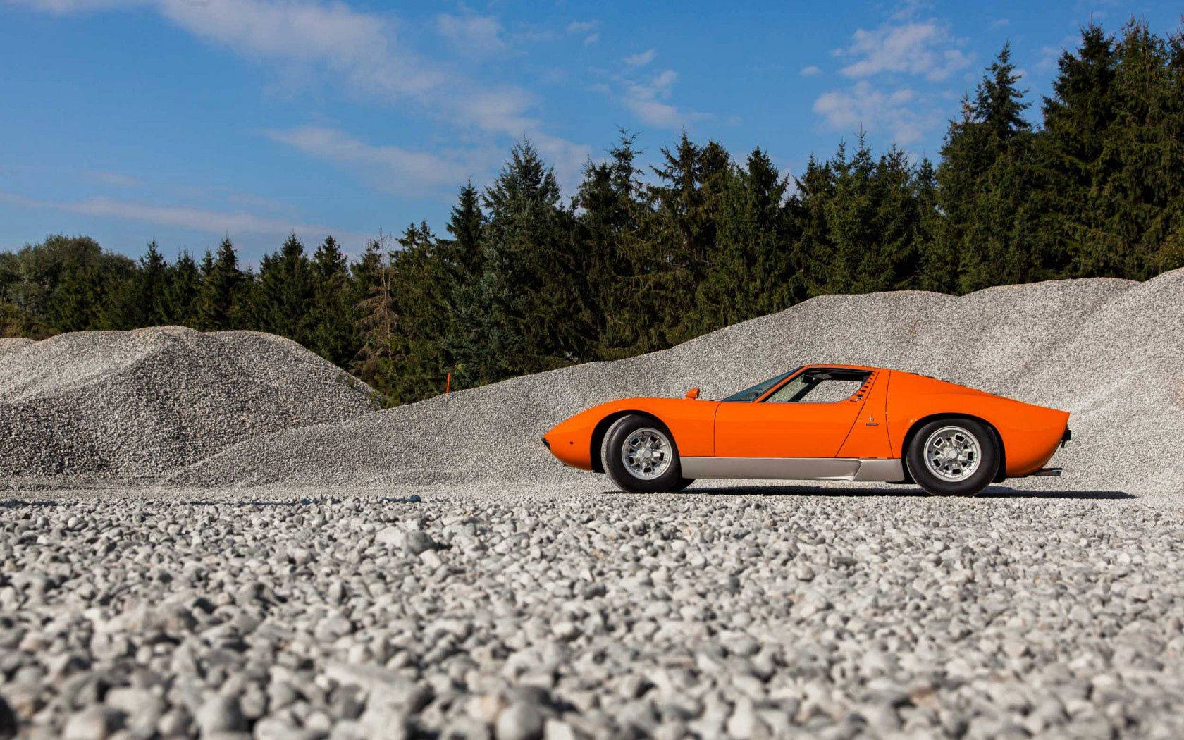 Oranje Lamborghini Miura op gruis agtergrond.