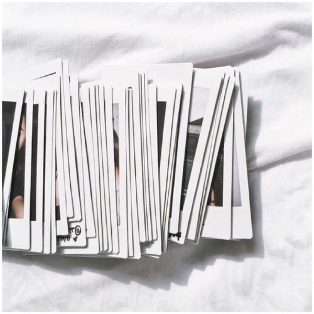 'n Stapel polaroidfoto's op 'n wit bed Muurpapier