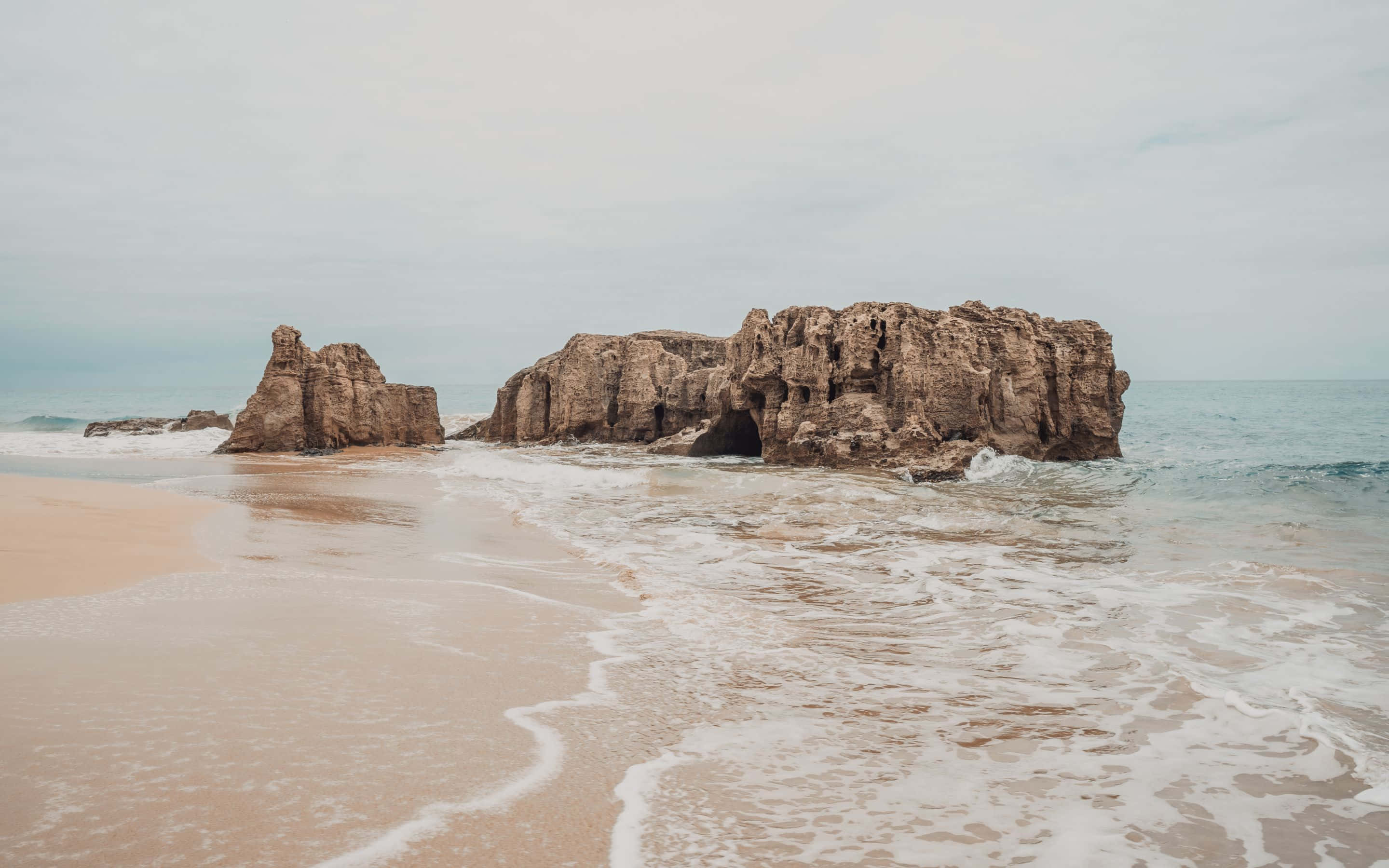 'n strand met rotse en golwe daarop Muurpapier