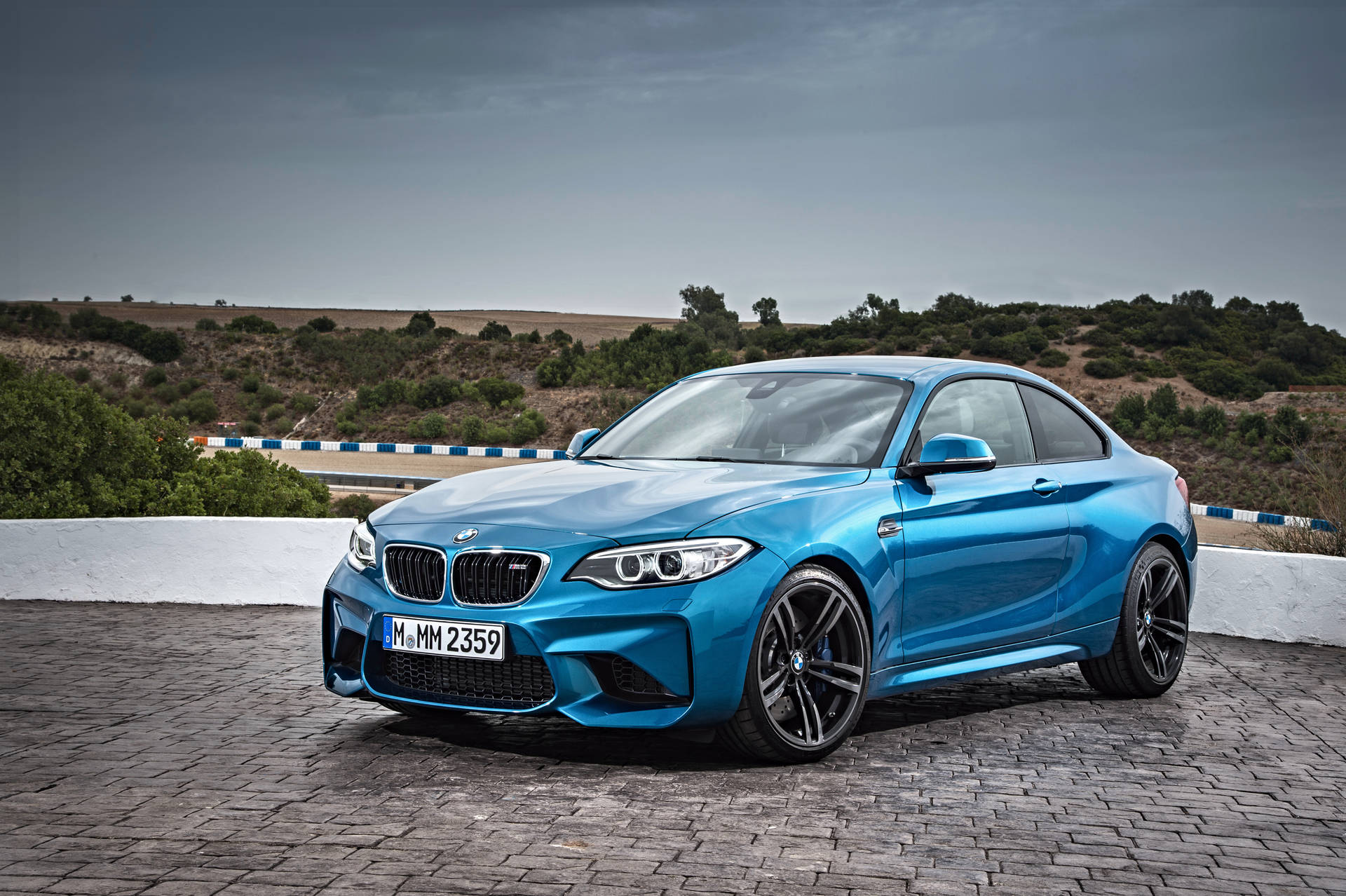 Blou BMW F87 op teerpad met berguitsig agtergrond