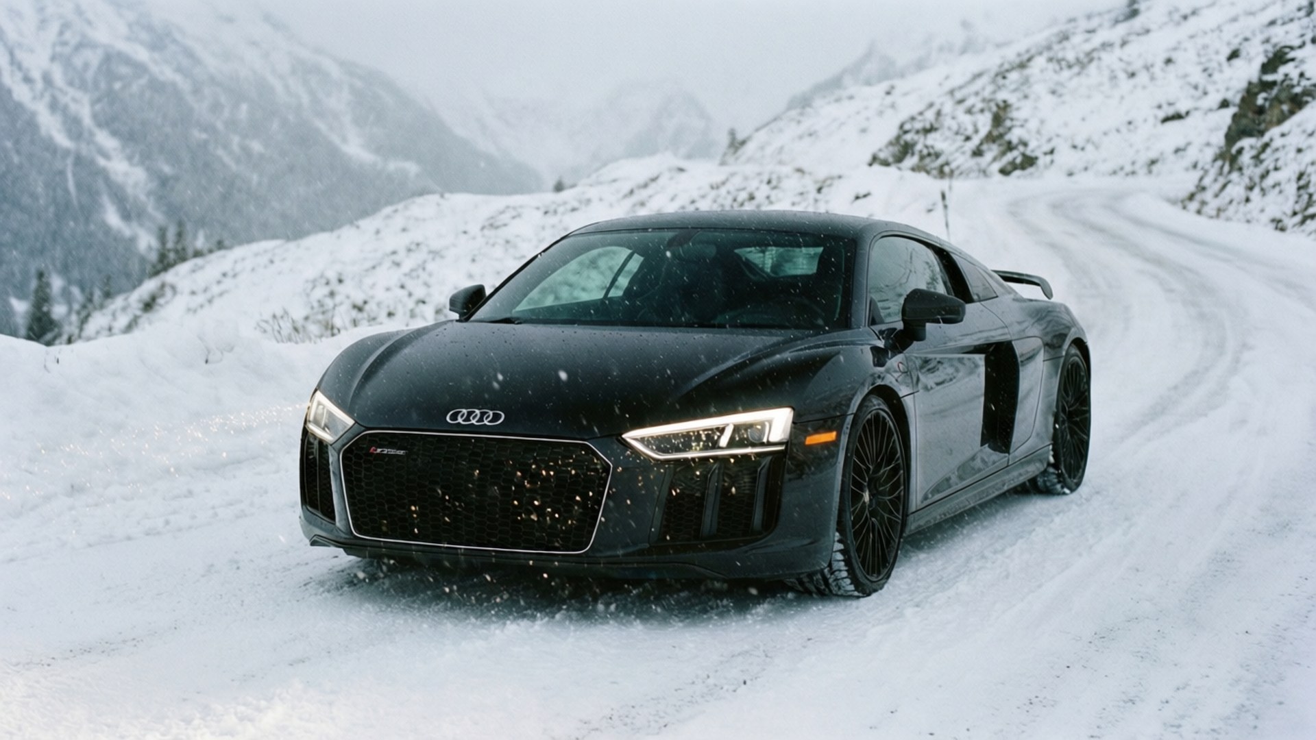 ’n Swart Audi R8 ry deur ’n sneeubedekte alpynse pad met vallende sneeu. — Koel motors Muurpapier