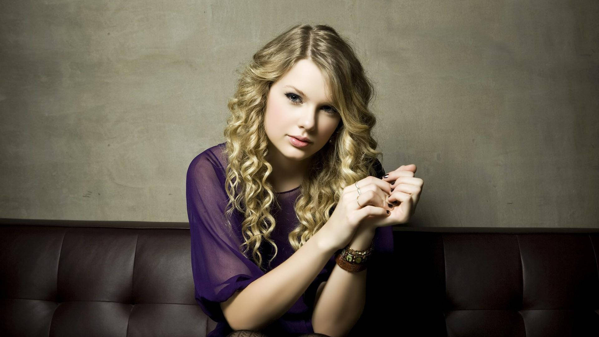 Sittende krulhare Taylor Swift in pers mesh-top agtergrond. — Taylor Swift Muurpapier