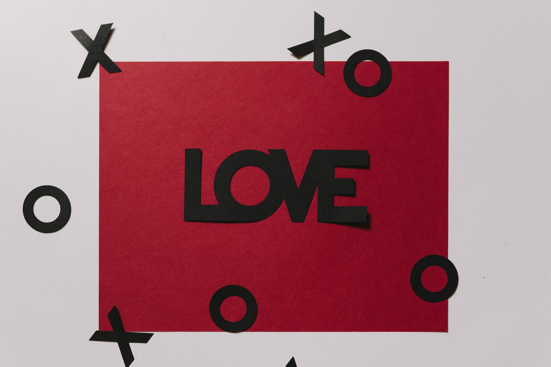 Rooi liefdesbrief met die inskripsie "Liefde" in swart en drywende uitsny van XOXO op wit oppervlak.