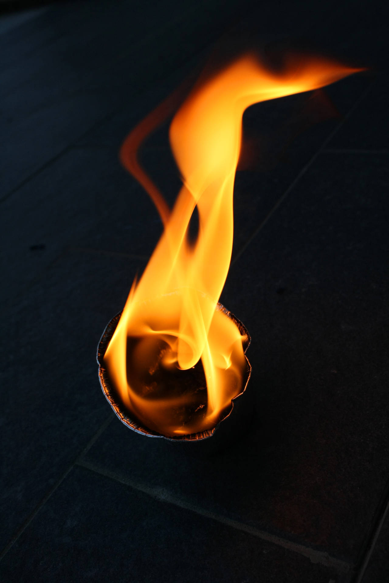 Ronde stuk papier wat op die vloer brand. Naby-skoot van vlam van vuur. Ding wat brand binne-in 'n donker kamer.