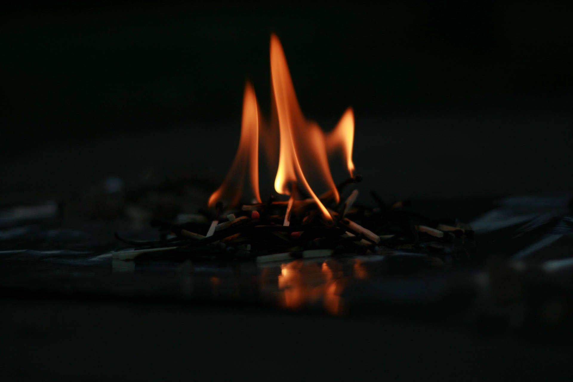 Klein vuurhoutjies aan die brand met dowwe helder rooi oranje vlamme op die vloer binne-in 'n donker kamer.