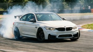 ’n Wit BMW M4 dryf om ’n draai op ’n renbaan met bandrook en bewegingsvervaging. — Bmw Muurpapier