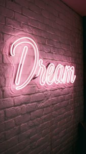 'n Ligpienk neonbord 'Droom' wat gloei teen 'n wit baksteenmuur, inspirerend en esteties. — Ligpienk estetika Muurpapier