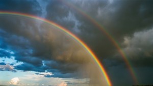Dubbel reënboog wat verskyn ná die storm met donker wolke op die agtergrond. — Luguitsig Muurpapier