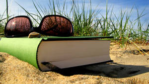 Somer vakansie met groen boek en sonbril op die sand.