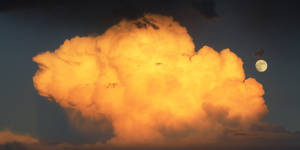 Maan en wolke wat die sonlig van sonsondergang weerkaats. Volmaan wat wys voordat die son ondergaan.