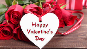 Boeket rooi rose wat op die tafel lê met 'n wit hartkaartjie wat sê "Happy Valentine's Day". — Studio Display Muurpapier
