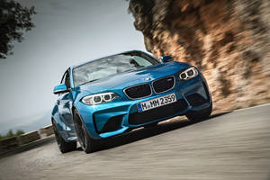 Blou BMW M2 F87 motor op pad langs berg agtergrond