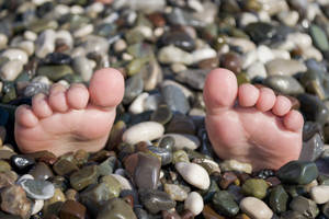 Voete op die rotse tydens somervakansie, snaakse situasie op strand met klippies.