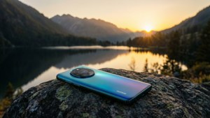 Huawei-foon op 'n rots wat uitkyk oor 'n bergmeer teen sononder, rustige landskap.