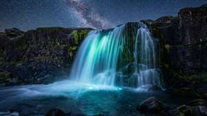 Lumineserende waterval onder 'n sterrehemel met diep swartes.