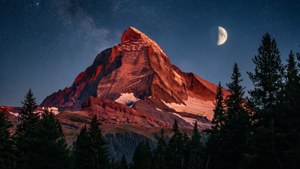 'n Majestueuse rooi bergpiek wat deur maanlig verlig word onder 'n sterrehemel.
