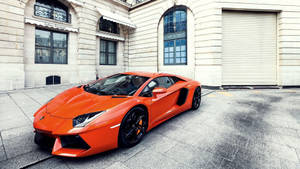Oranje Lamborghini Aventador met gebou-agtergrond.