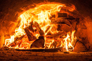 Kaggel met brandende hout en helder gloeiende vlamme binne-in 'n ou klein vuurmaakhoutgrot.